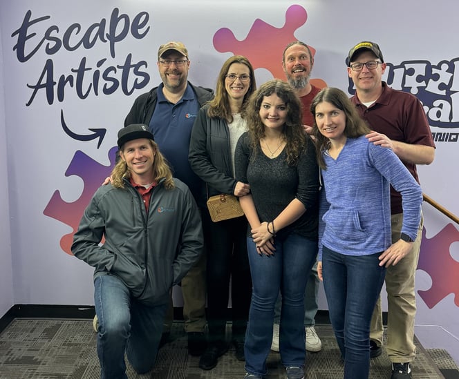 Dymaptic team members in front of an escape room mural